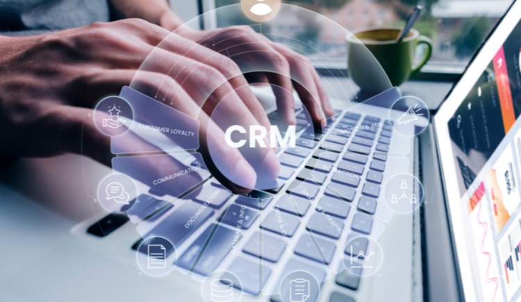Hands typing on a laptop with a digital ‘CRM’ interface overlay.