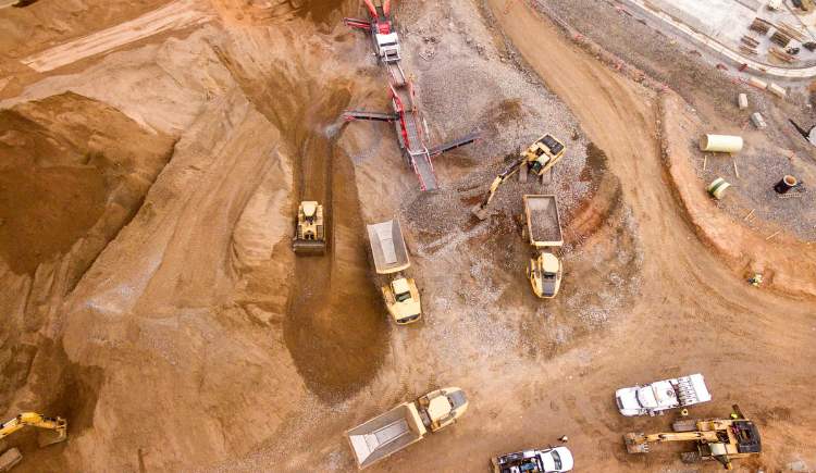 Aerial view of a construction site with heavy machinery, including excavators, dump trucks, and loaders working on moving dirt and gravel.
