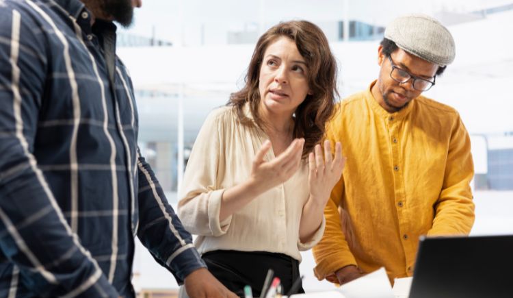 Coworkers discussing documents at a table with a laptop.