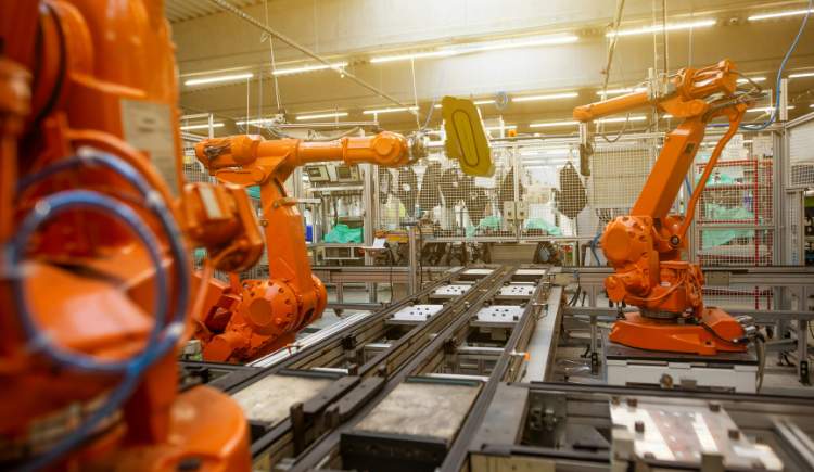 Orange robotic arms work along a conveyor in a brightly lit automated factory.